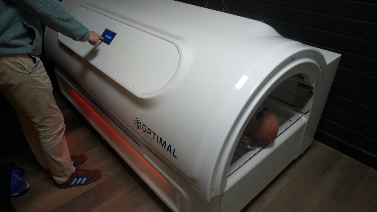A staff member's hand on the infrared bed's control panel, a client already lying inside the open end