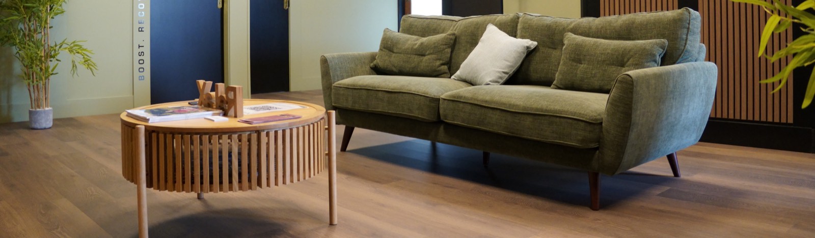 The lounge at the clinic: a green sofa, a slatted table and bamboo against the treatment-room doors