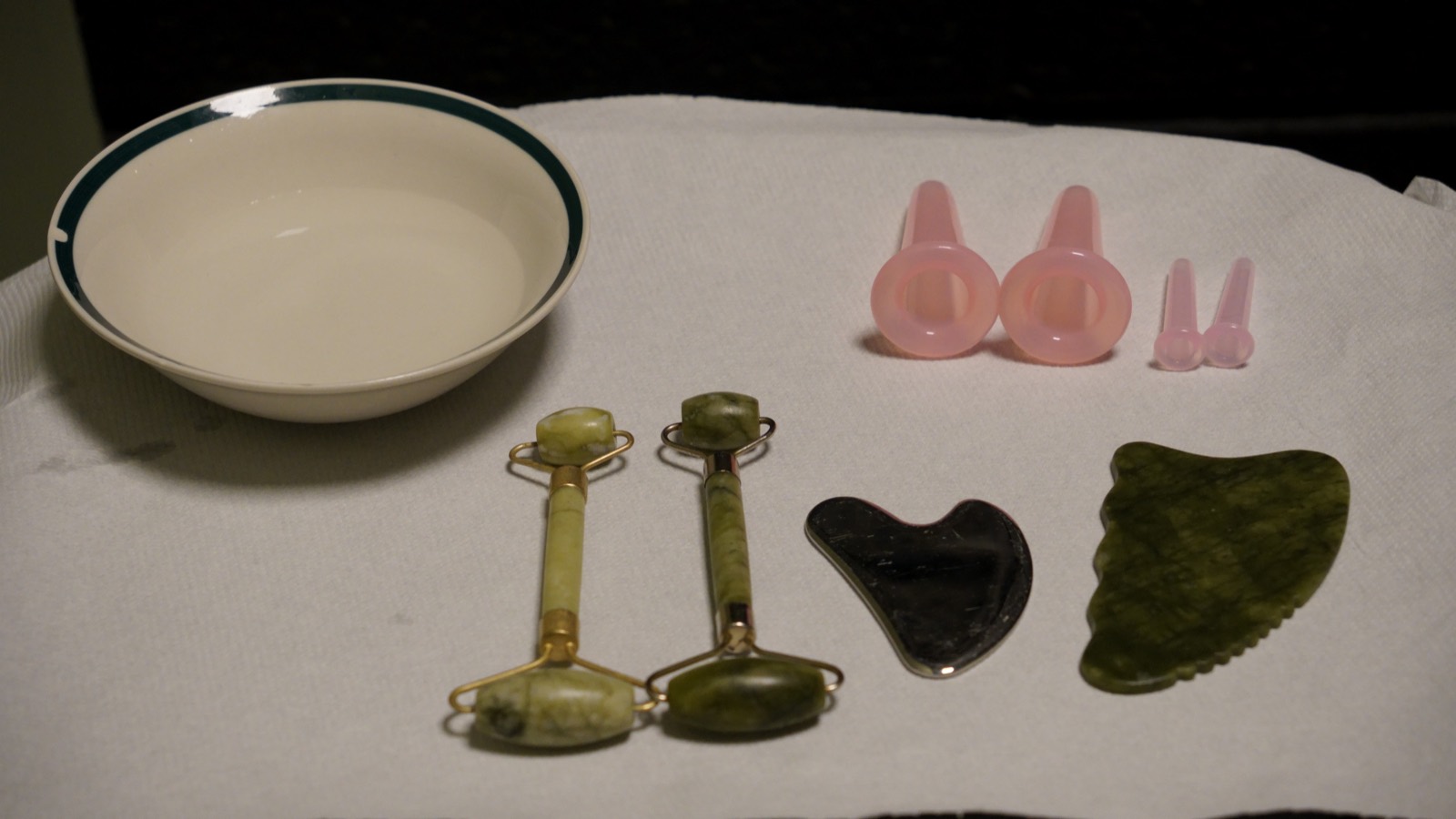 Jade rollers, gua sha stones and facial cupping bulbs laid out on white linen