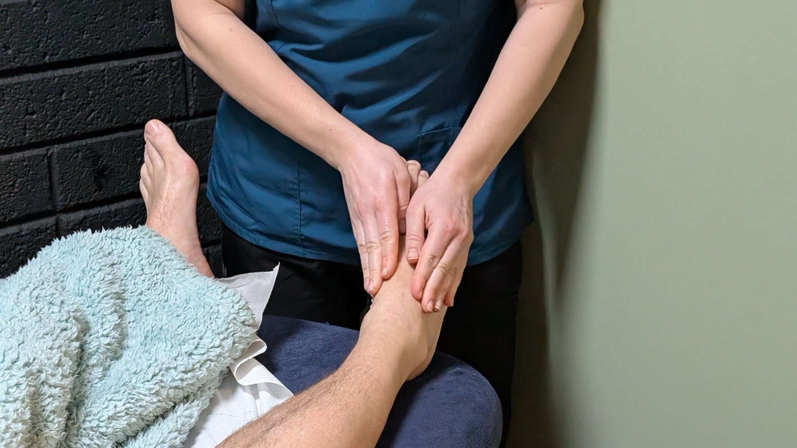 A therapist's hands working a client's foot and ankle