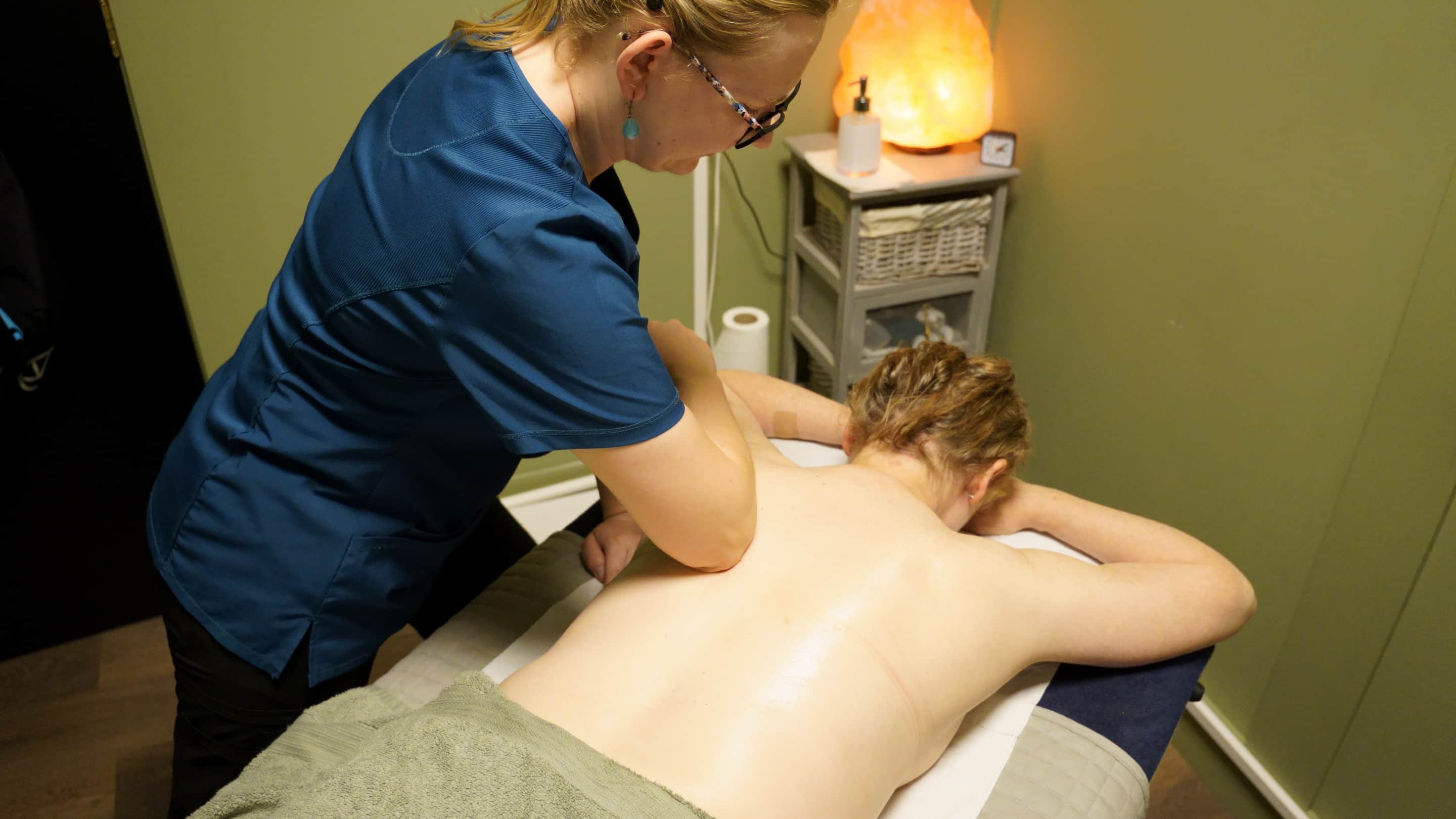 A therapist working a client's back in the olive treatment room at the Clonmel clinic, a salt lamp on the shelving behind