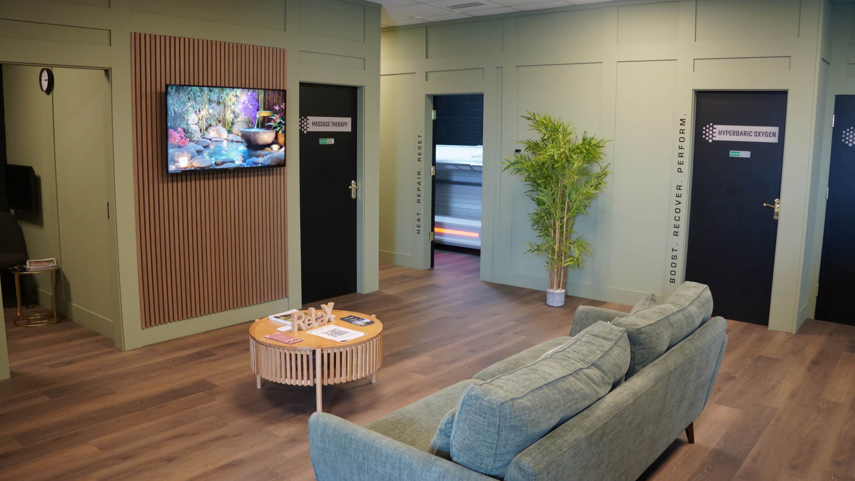 The waiting area at Optimal Health and Recovery, Ard Gaoithe Business Park, Clonmel: sofas, the massage and hyperbaric oxygen room doors, and an open door onto the lit infrared bed